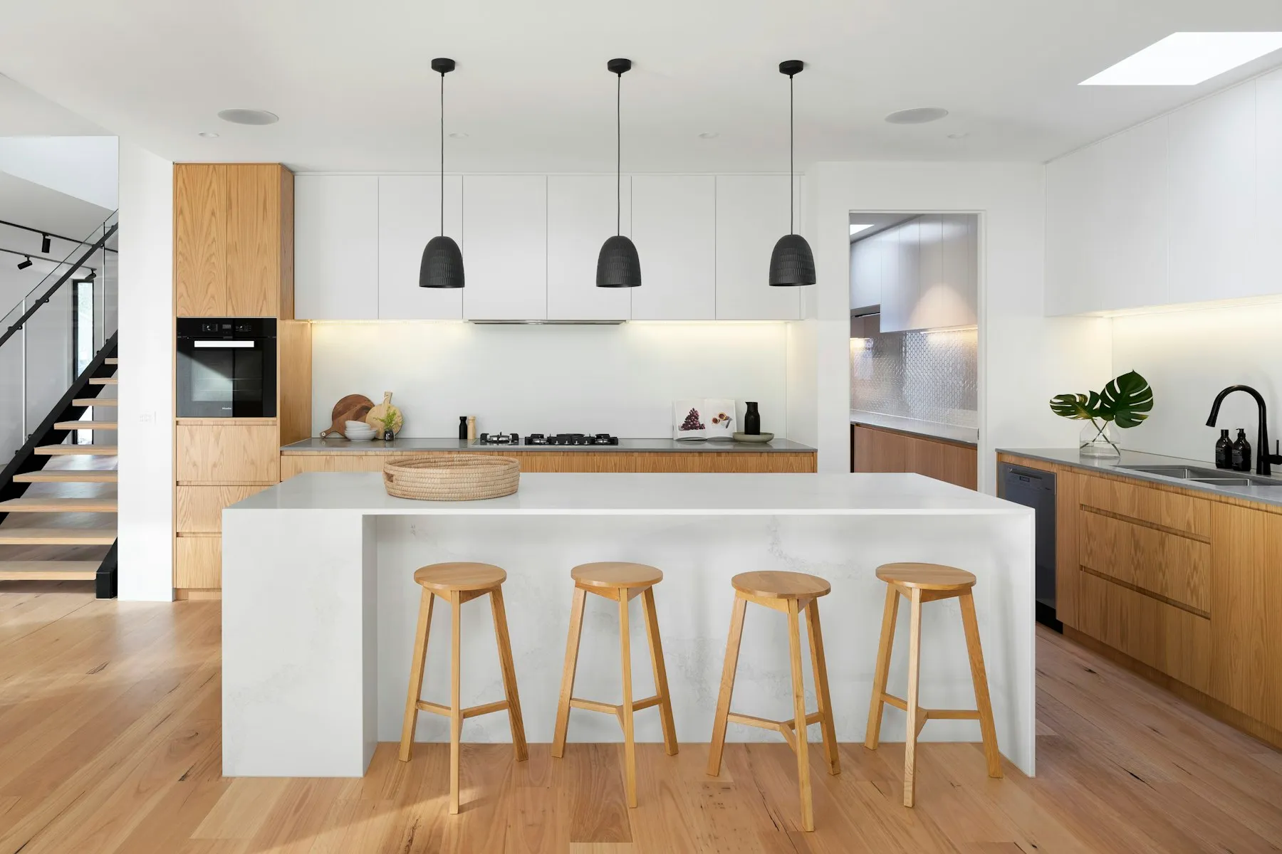 Cuisine ouverte blanche avec îlot central, tabourets en bois et suspensions noires